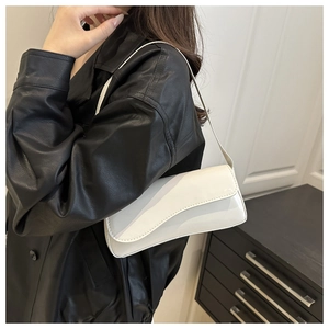 Close-up of white patent leather baguette bag with a modern curved flap on a model