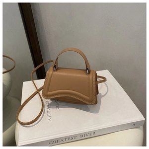 Close-up of a minimalist camel leather handbag with unique curved stitching and silver hardware