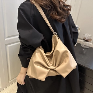 Model wearing a beige bow-knot shoulder bag with crescent shape and chic pleated details