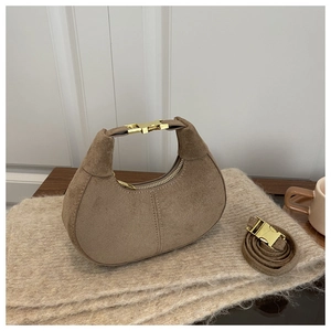 Détail d'un sac demi-lune en daim marron avec fermoir doré et une ambiance hivernale
