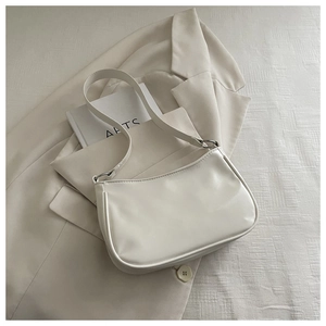 Close-up of minimalist white leather baguette bag with metal rings on beige blazer