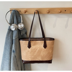 Détail du sac cabas camel texturé avec des lanières en cuir verni marron foncé au mur