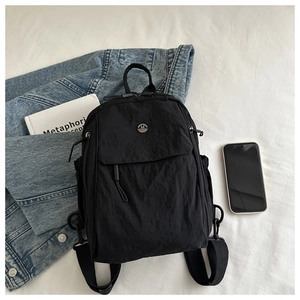 Flat lay of a black nylon backpack with metal M logo, denim jacket and book props