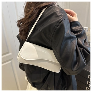 Minimalist white patent leather baguette bag with wavy flap detail shown on shoulder