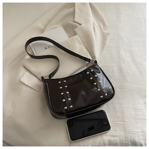 Detail of dark brown leather crossbody bag with silver studs on a beige blazer background