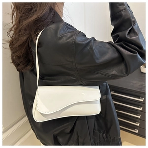 Close-up of a white patent leather shoulder bag with unique curved flap and minimalist design