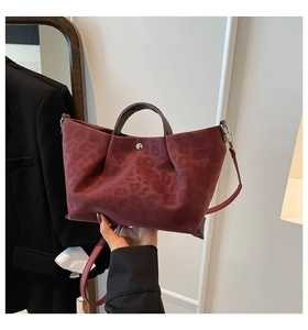 Detail of burgundy tote bag with subtle leopard pattern and silver metal fasteners