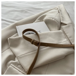 Detail showing a slim brown leather belt with a rectangular metal buckle on a beige blazer