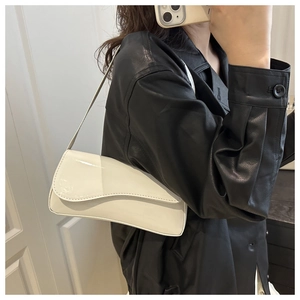 Close-up of white glossy patent leather crossbody bag with asymmetric curved flap