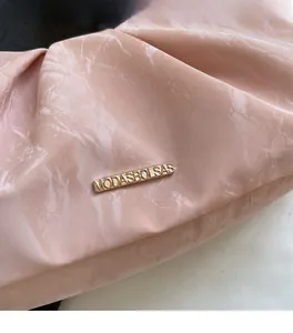 Dettaglio borsa a nuvola rosa con trama marmorizzata, logo in metallo dorato e pieghe morbide