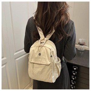 Model wearing a lightweight cream nylon backpack with side pockets and a metal logo