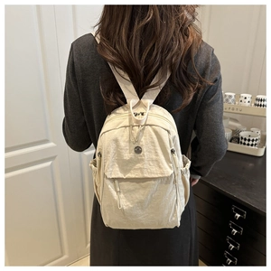 Rear view of model wearing a cream oxford fabric backpack with multiple utility pockets