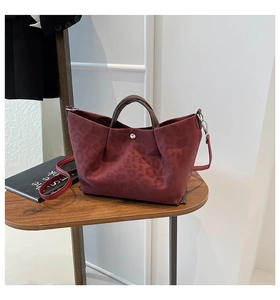 Detail of burgundy leopard print tote bag with silver buckle on a wooden table