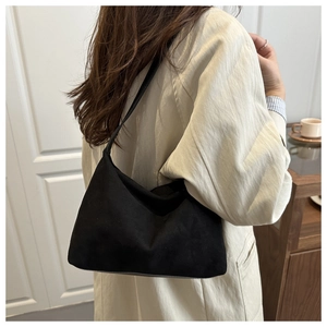 Detail view of a black matte suede shoulder bag paired with a beige trench coat