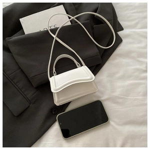 Detailed view of white micro bag with curved flap next to a smartphone for size reference