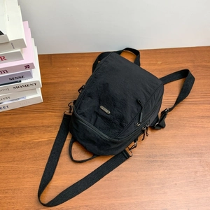 Detail of a black tear-resistant nylon mini backpack with multiple zipper pockets on wood