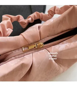 Dettaglio della cerniera in metallo dorato scorrevole su una borsa rosa a pieghe