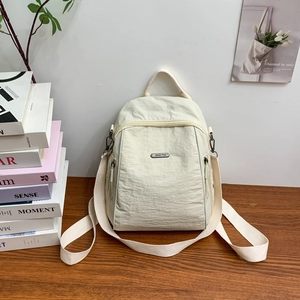 Detailansicht eines cremefarbenen Nylon-Rucksacks mit silbernem Metall-Logo auf Holztisch