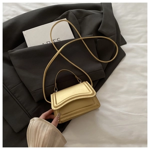 Detail of a mini gold handbag with pearlescent finish on a grey suit and book background