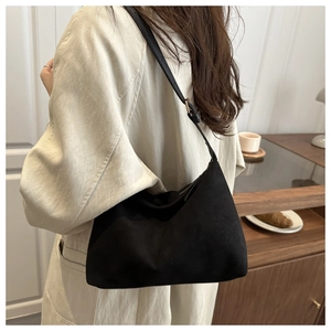 Detail of a vintage black suede shoulder bag with adjustable strap worn by a model