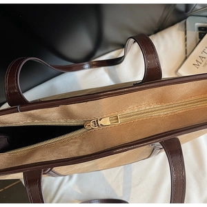 Vue détaillée du sac cabas en toile beige avec bordure en cuir brun et zip doré brillant