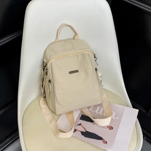 Close-up of beige nylon backpack with multi-compartment zippers and adjustable straps