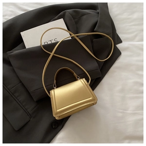 Macro shot of metallic gold PU leather handbag with fine stitching on dark grey blazer