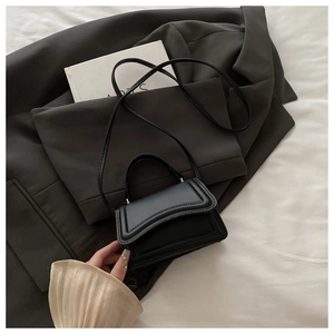 Detail of a black mini matte leather crossbody bag with top handle on a gray blazer