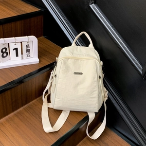 Detail view of large cream nylon travel backpack on wooden stairs showing metal logo plate