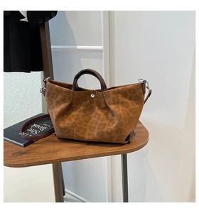 Detail of leopard print tote bag with brown leather handles on a wooden table