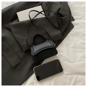 Detail of black mini crossbody bag with embossed contours on elegant grey blazer