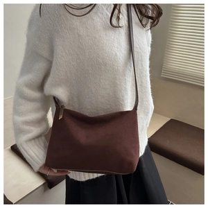 Close-up of a minimalist dark brown suede crossbody bag worn with a cream knit sweater