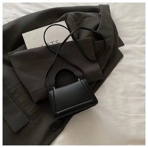 Minimalist black leather crossbody bag displayed on a grey blazer with artistic book details