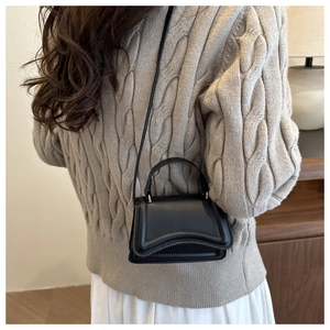 Detail of black mini crossbody bag with wavy texture against a cream knitted sweater