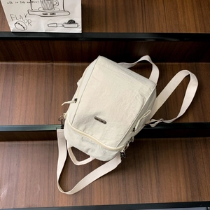 Dettaglio dello zaino in nylon crema con trama stropicciata e placca logo in metallo