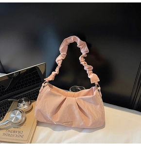 Detailed view of pink ruched leather handbag with ruffled strap and gold metal logo bar