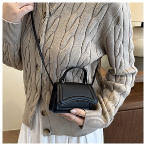 Detail of a black mini flap bag worn over a beige knit cardigan for size reference