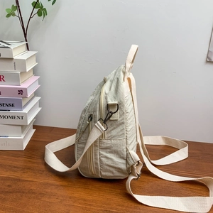 Dettaglio laterale di uno zaino in nylon beige con cerniere laterali e trama del tessuto