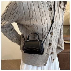 Detail of a black mini crossbody bag featuring a unique wave-edge flap and top handle design