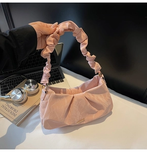 Close-up of pink pleated shoulder bag with gold logo plate and scrunchie handle