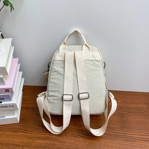 Dettaglio zaino in tela verde chiaro con spalline beige su un tavolo in legno