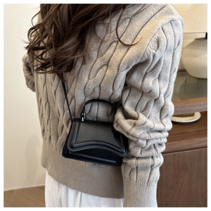 Detail of a black leather handbag with a curved base and structured flap worn cross-body