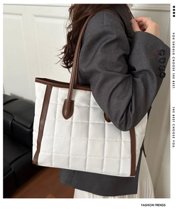 Detail of large quilted white tote bag with brown leather trim shown on model shoulder