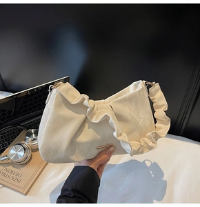 Detail view of cream pleated handbag with metallic logo tag and textured handle design