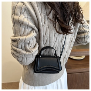 Close-up of minimalist black micro square bag with silver hardware on beige sweater