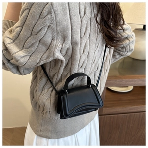 Chic black handbag with a wave curve flap worn with a beige sweater and white skirt