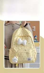 Detail view of beige polka dot backpack with white plush bow and soft hanging ornament