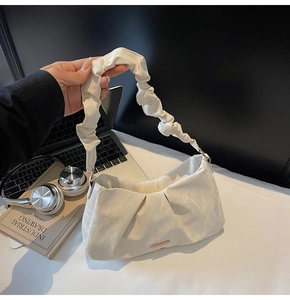 Detail of off-white pleated cloud bag with gold logo on a modern lifestyle desk