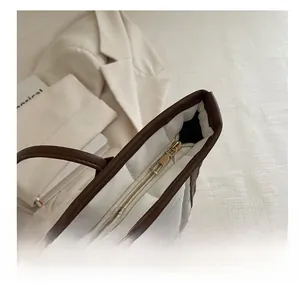 Detail view of smooth golden zipper closure on a white and brown quilted tote bag