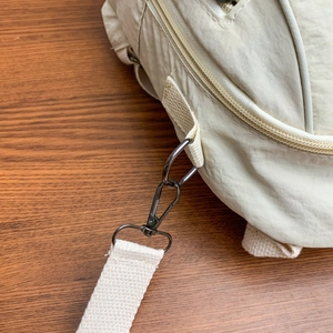 Dettaglio ravvicinato della borsa in nylon beige con gancio girevole in metallo nero e tracolla
